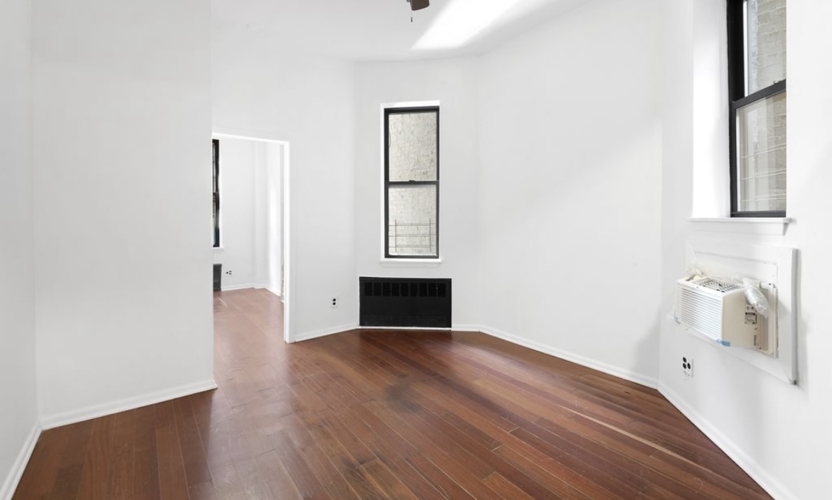 an empty room with wooden floor cabinet and windows