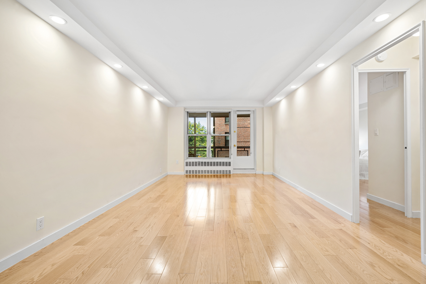 a view of an empty room with wooden floor and a window