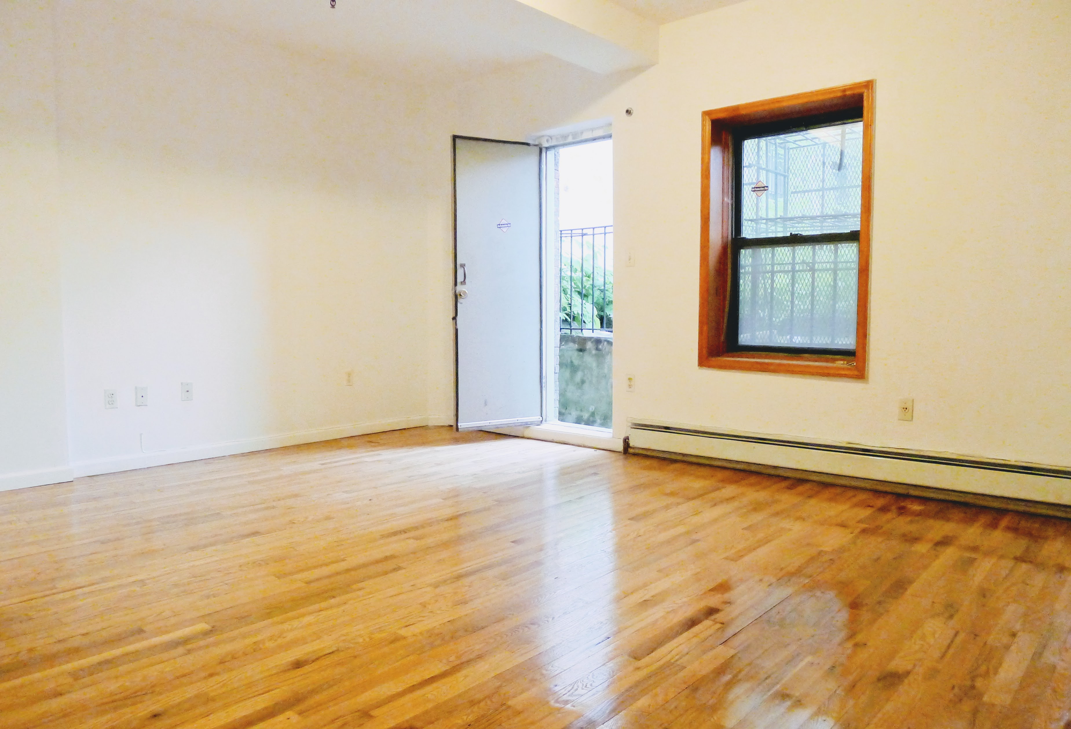 a view of an empty room with wooden floor and a window