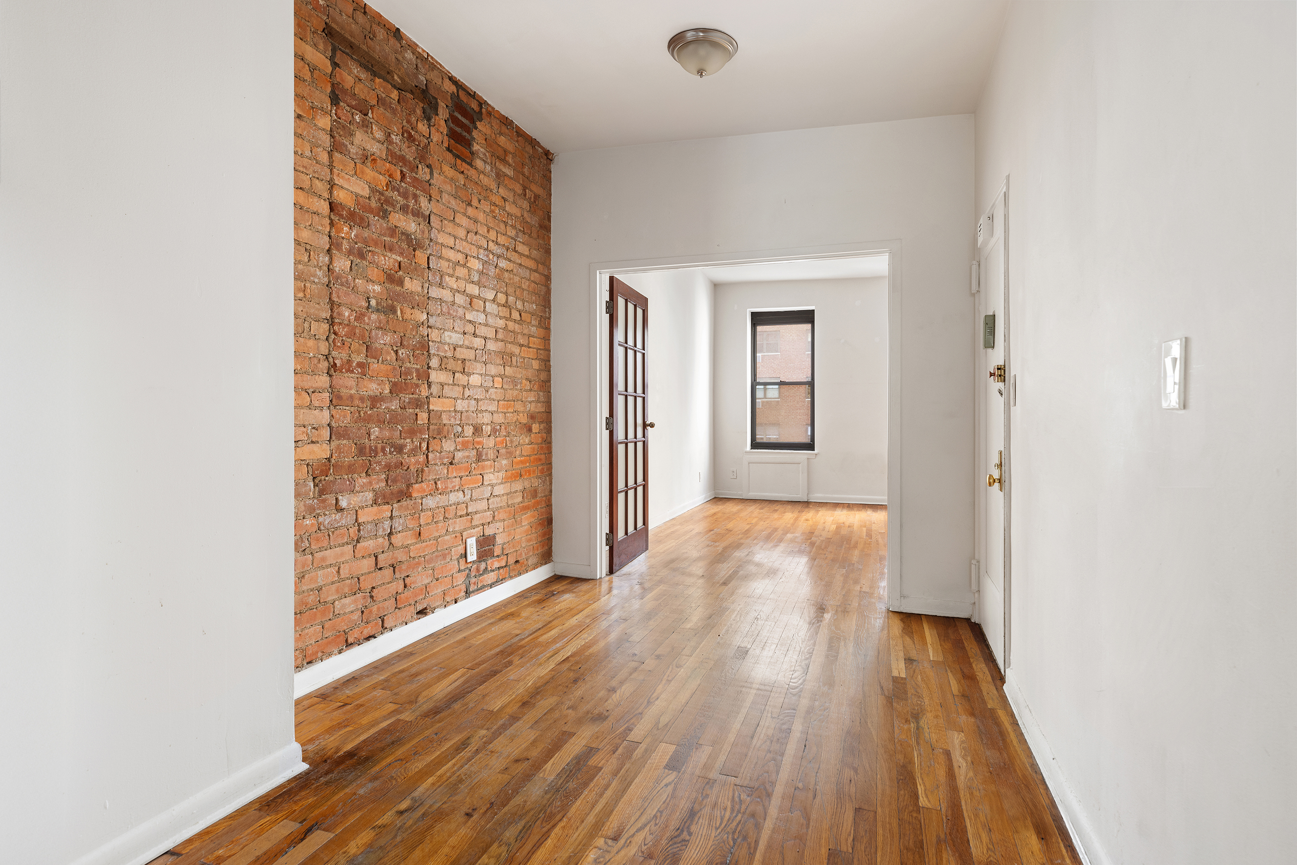 a view of a hallway with wooden floor and a bathroom