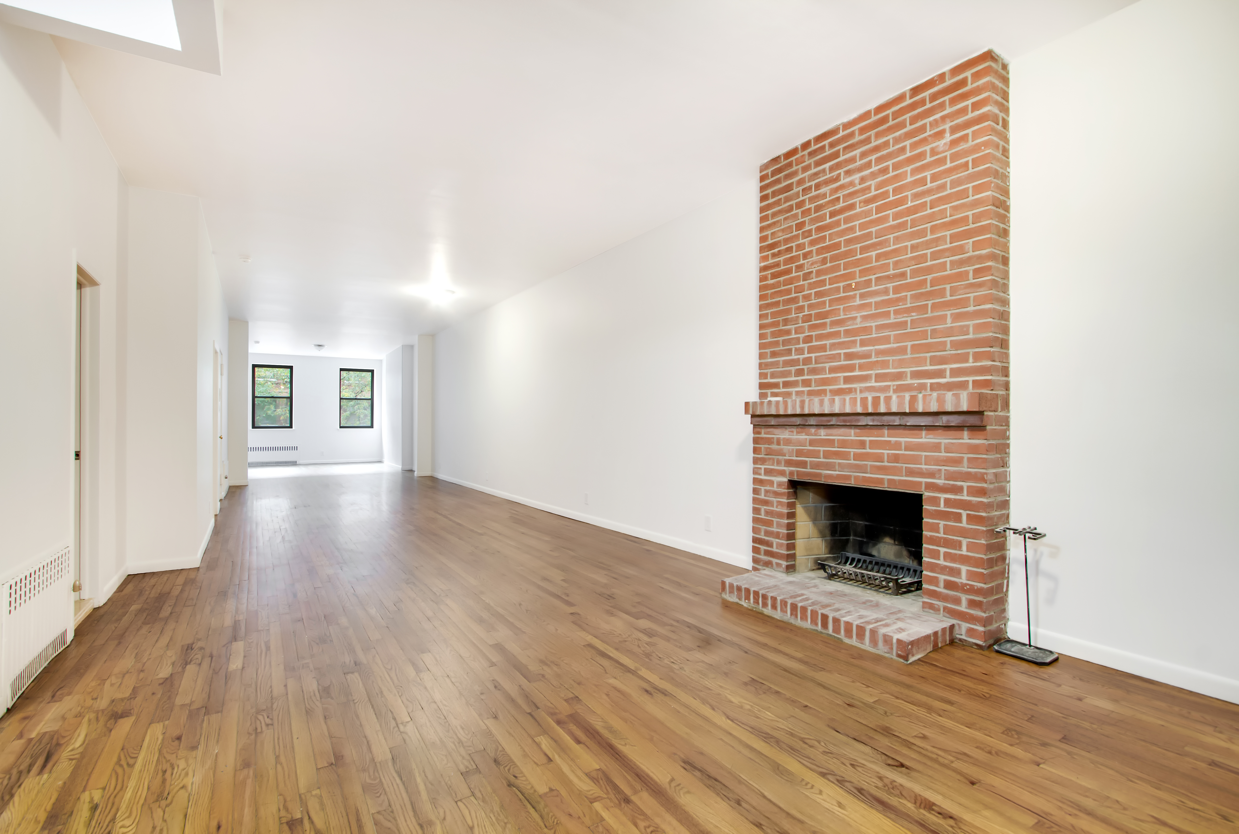 a view of an empty room with wooden floor fireplace and a window