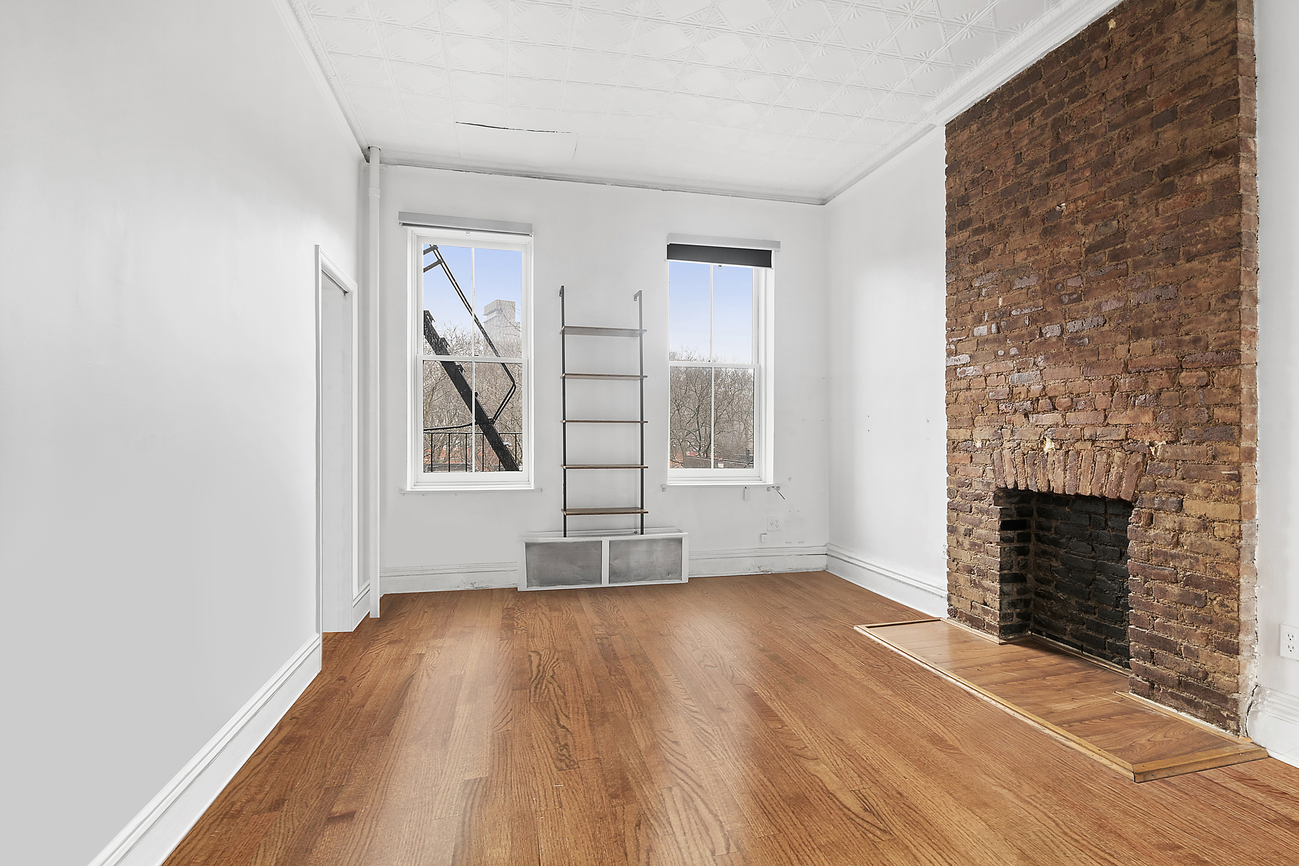 an empty room with wooden floor fireplace and windows