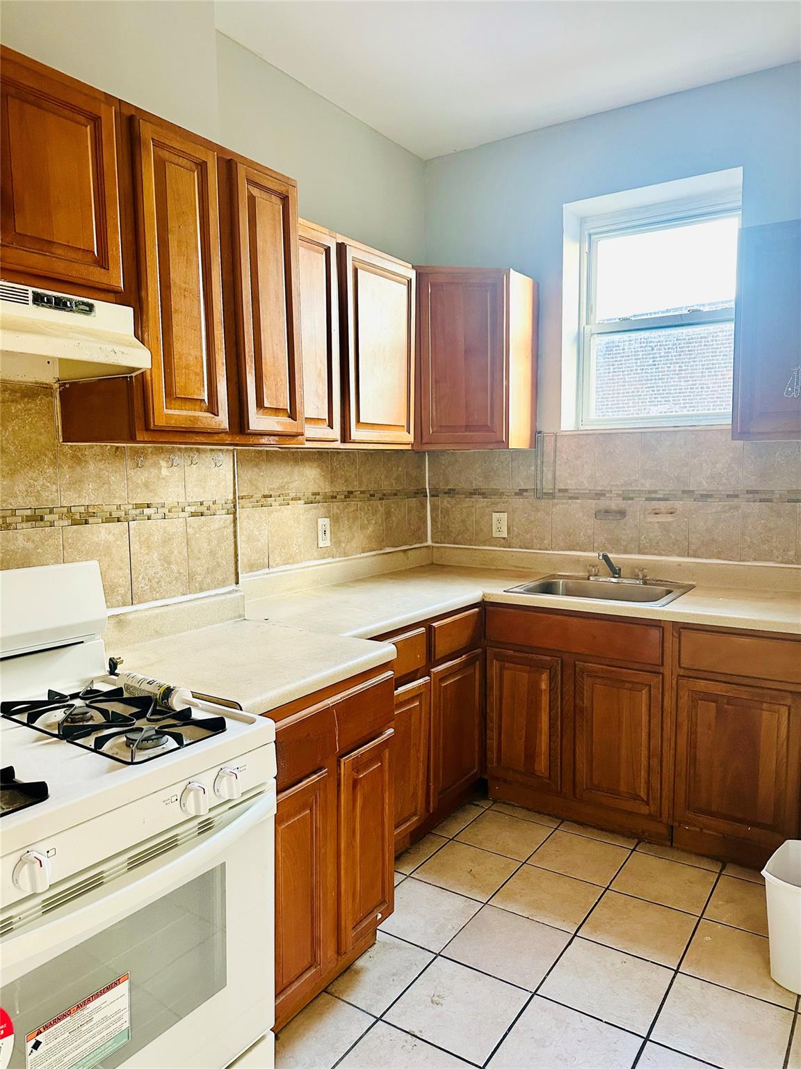 Kitchen featuring white gas range, decorative backsplash, sink, and light tile patterned floors