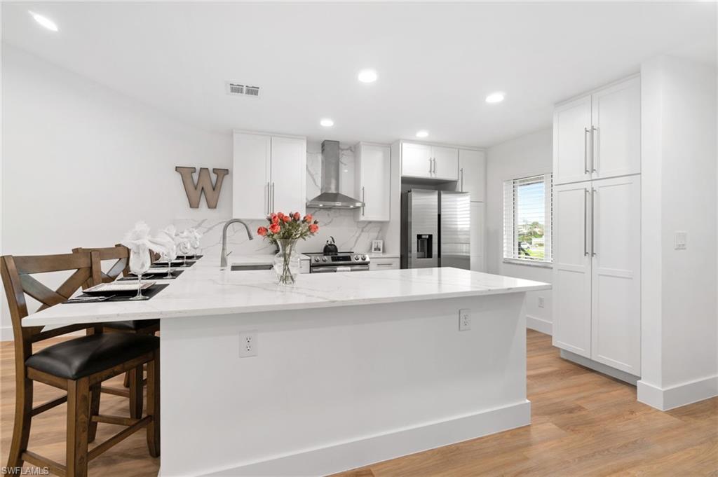 Kitchen featuring kitchen peninsula, white cabinetry, wall chimney exhaust hood, and stainless steel appliances