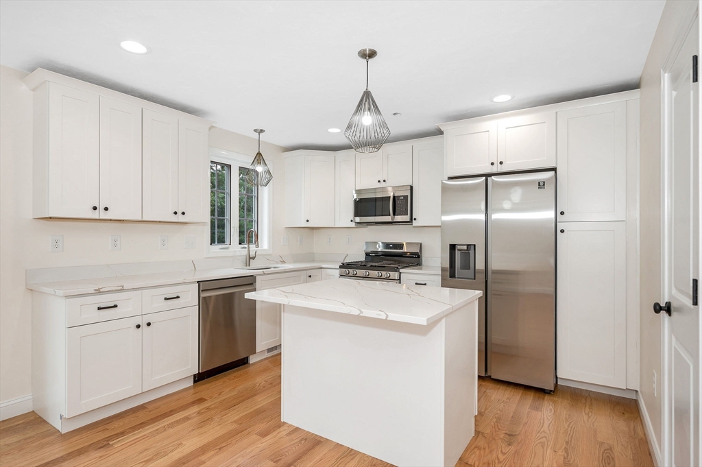 a kitchen with stainless steel appliances granite countertop a refrigerator a sink dishwasher a stove top oven a refrigerator and white cabinets with wooden floor