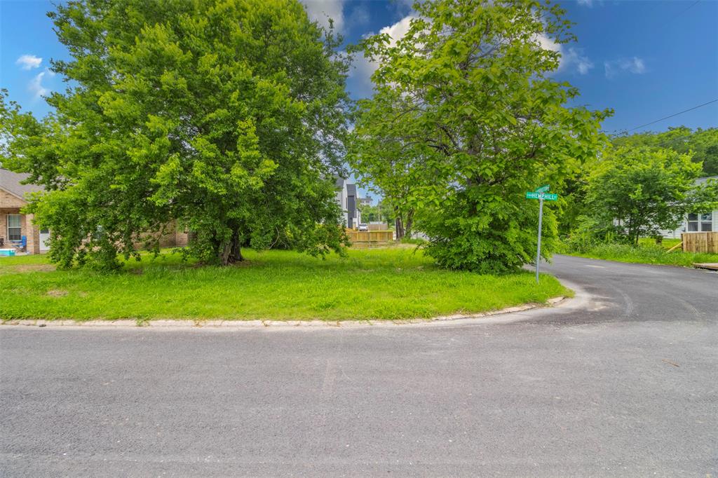 a view of a road with a big yard and large trees