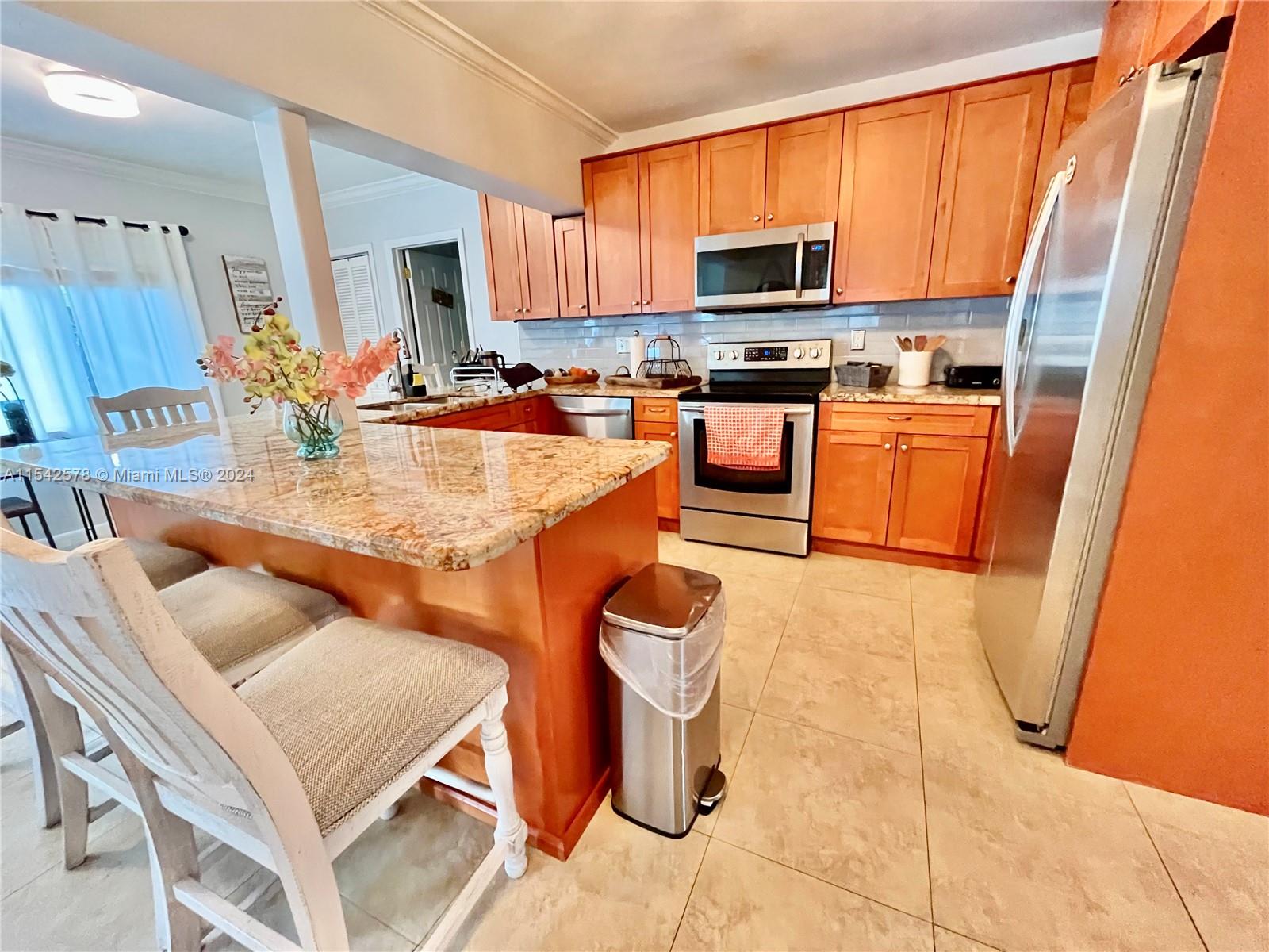 a kitchen with stainless steel appliances kitchen island granite countertop a refrigerator a stove a sink dishwasher and white cabinets with wooden floor