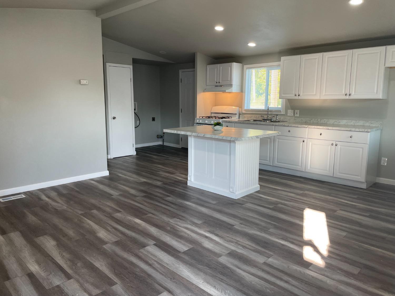 a kitchen with granite countertop a stove a sink and white cabinets with wooden floor