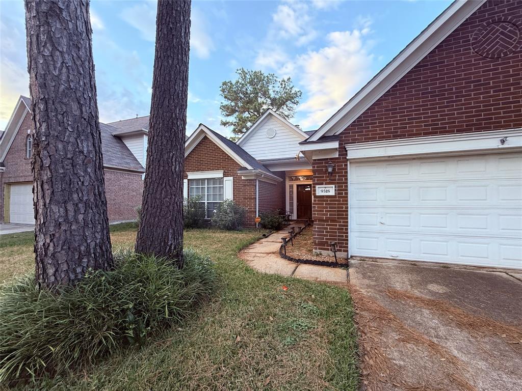 Quaint and cozy single-story brick home featuring a two-car garage, mature trees in the front yard, and a well-maintained lawn. The residence conveys a warm and inviting atmosphere with its classic design.