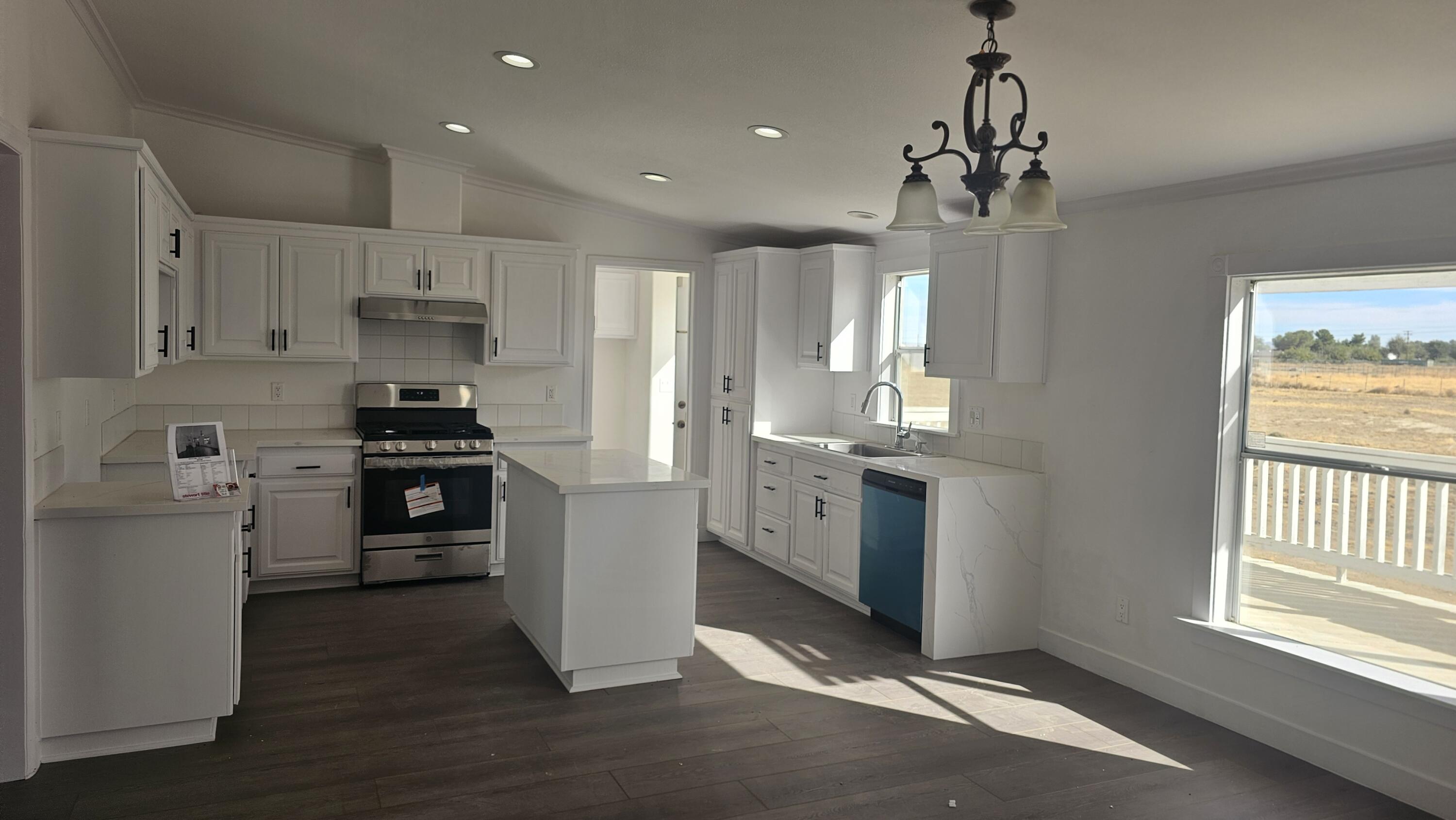 a kitchen with stainless steel appliances kitchen island granite countertop a refrigerator a sink dishwasher a stove and white cabinets with wooden floor