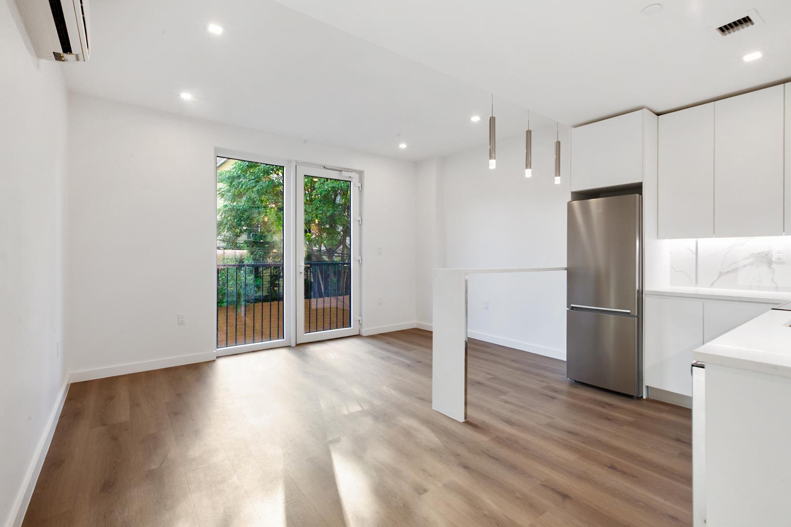 a view of an empty room with wooden floor and a kitchen