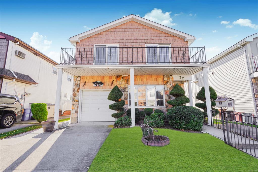 View of front of property featuring a balcony, a garage, and a front lawn