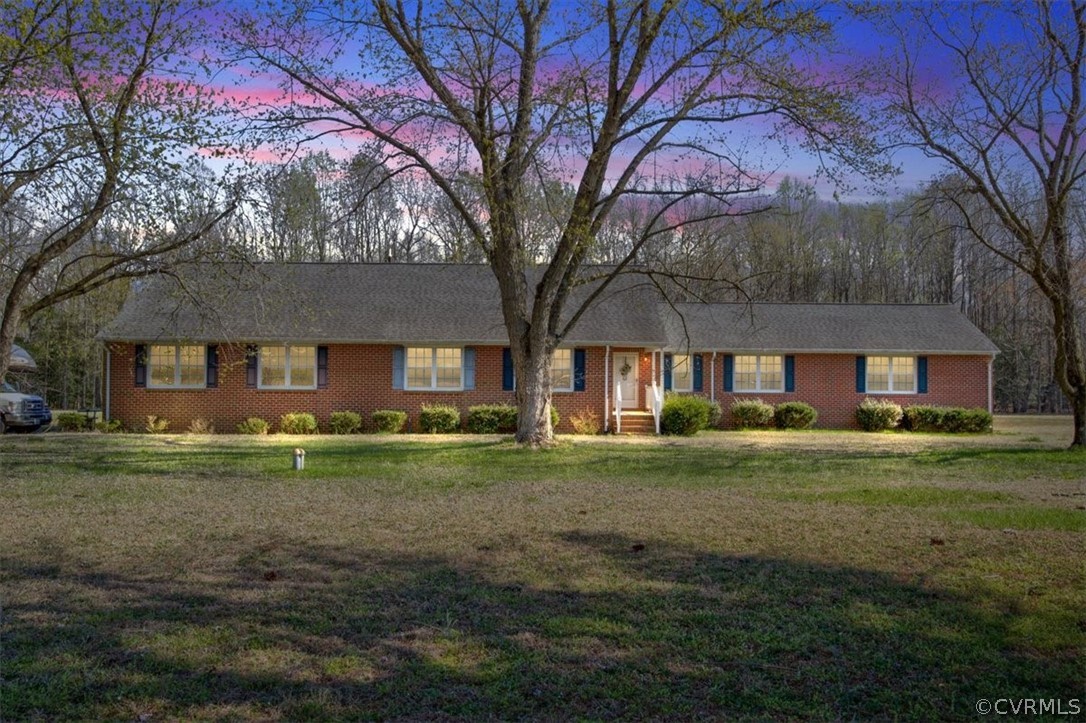 a view of a big yard in front of a brick house with a large tree