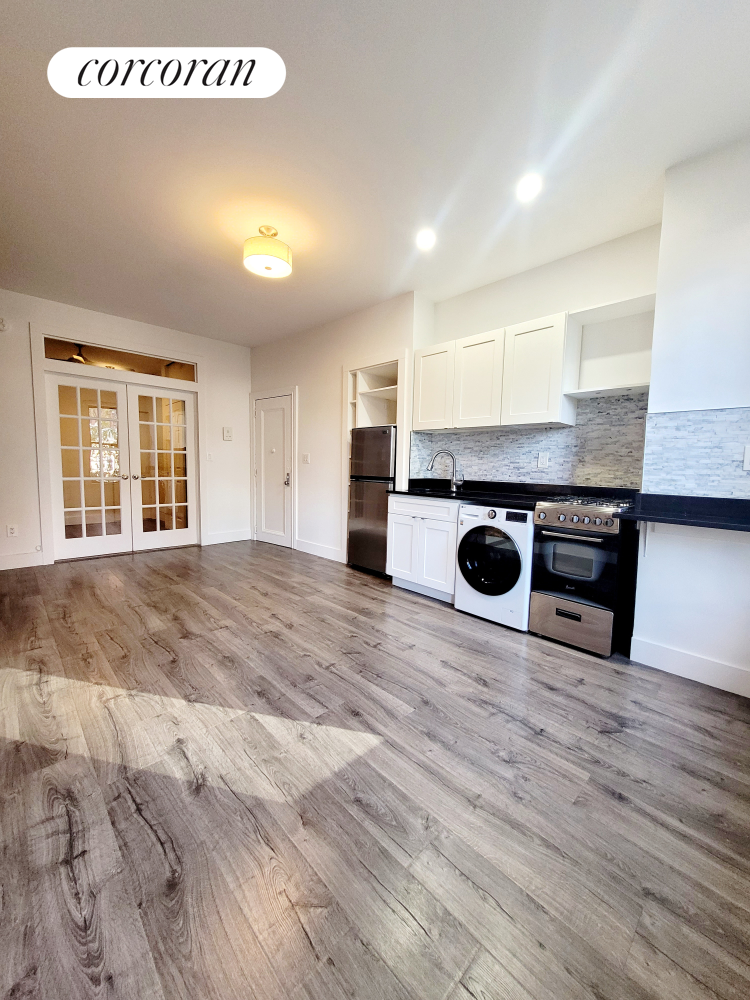 an empty room with wooden floor kitchen view and windows