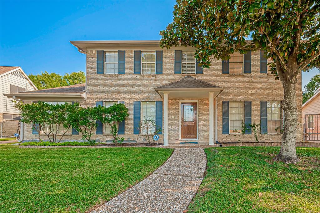 Charming two-story brick home boasts a welcoming walkway, a manicured lawn, and mature trees that add character and elegance.