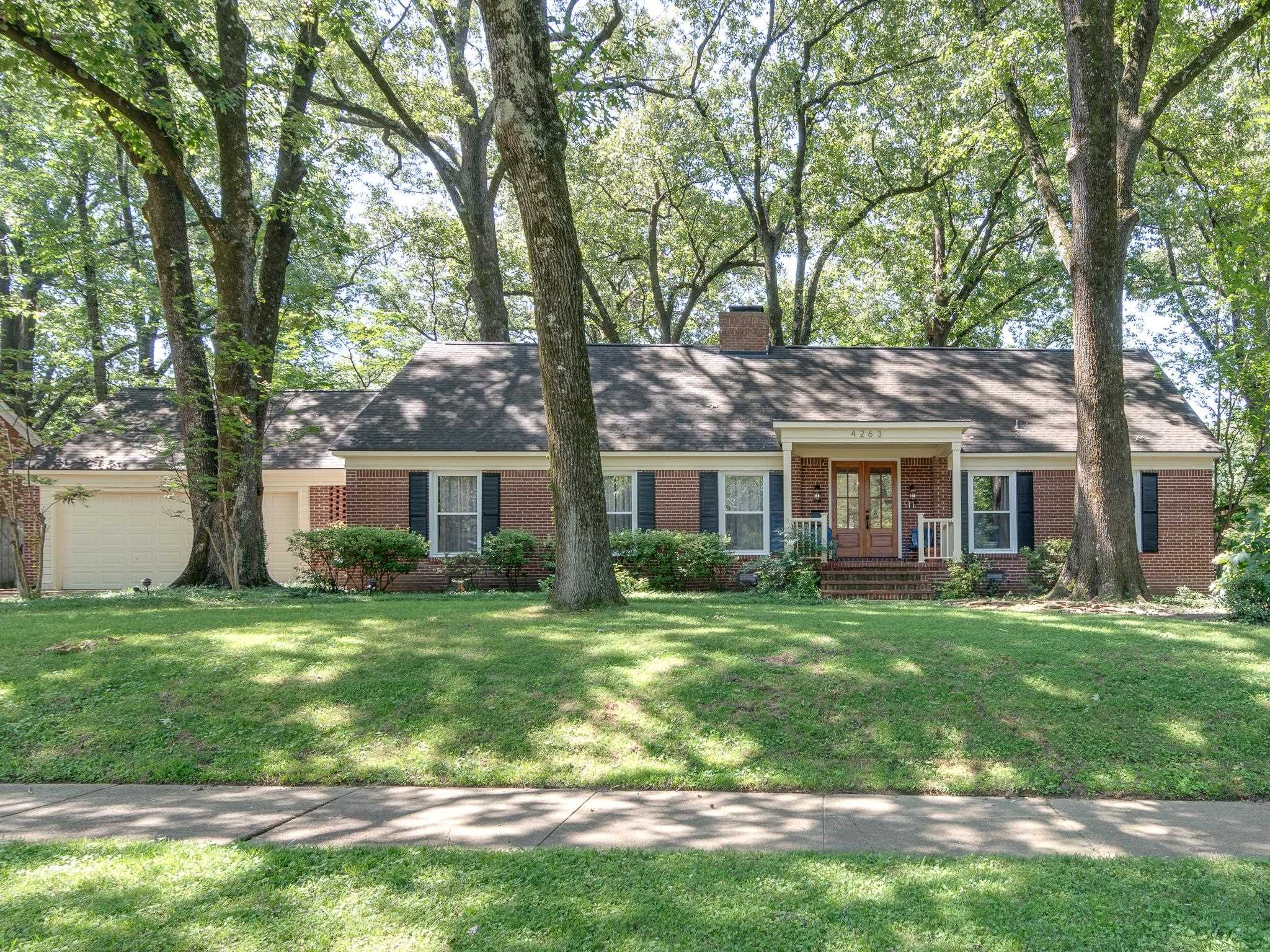 a view of a yard in front of a brick house with a big yard and large trees