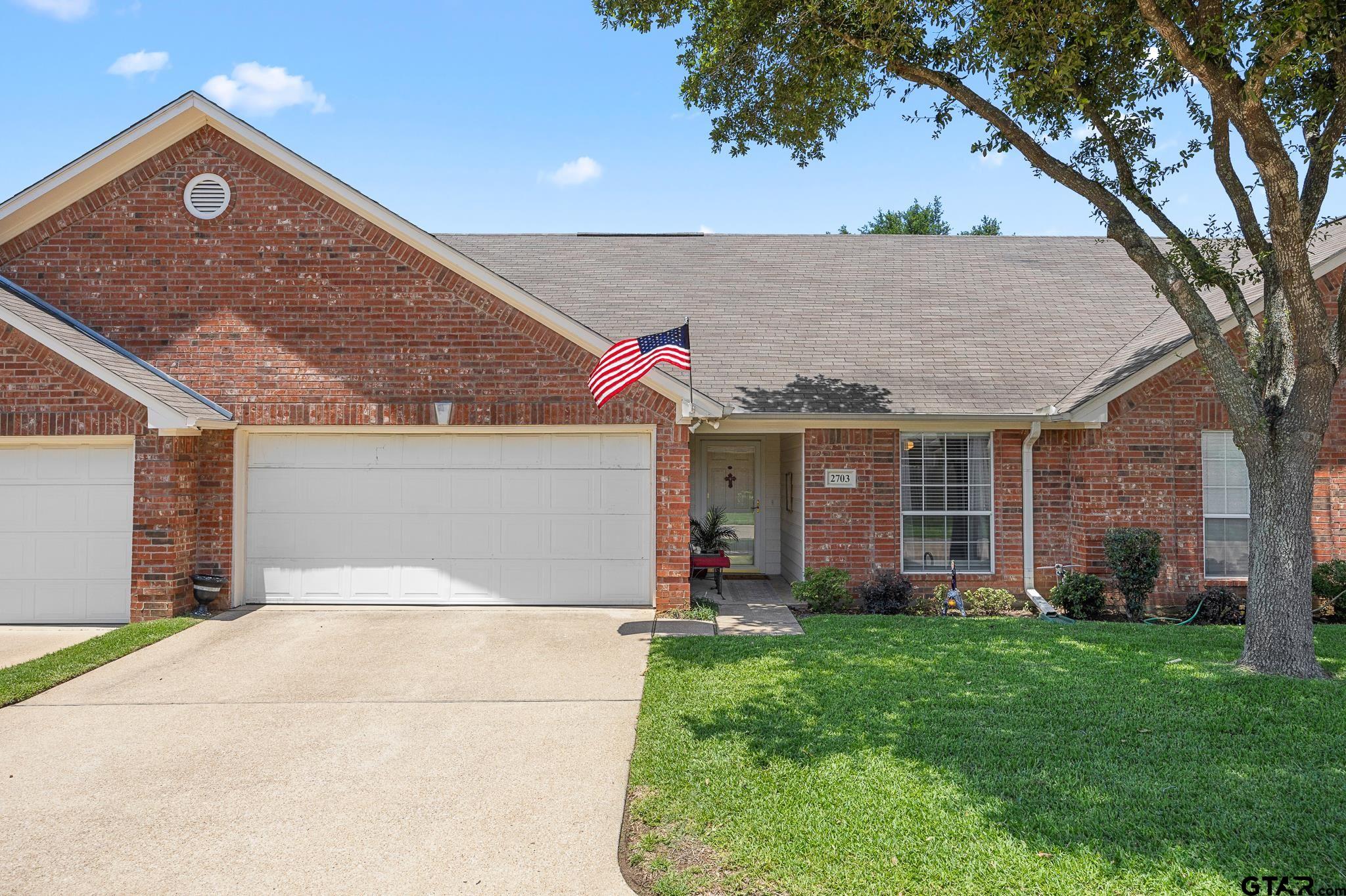 a view of a house with brick walls and a yard with a large tree