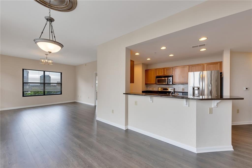 a view of kitchen with stainless steel appliances granite countertop a stove top oven a refrigerator and a wooden floor