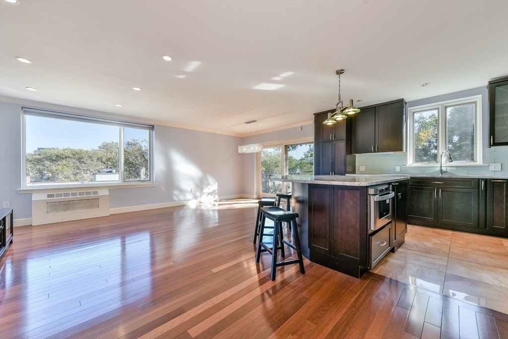 a kitchen with kitchen island granite countertop a stove a sink a dining table and chairs with wooden floor