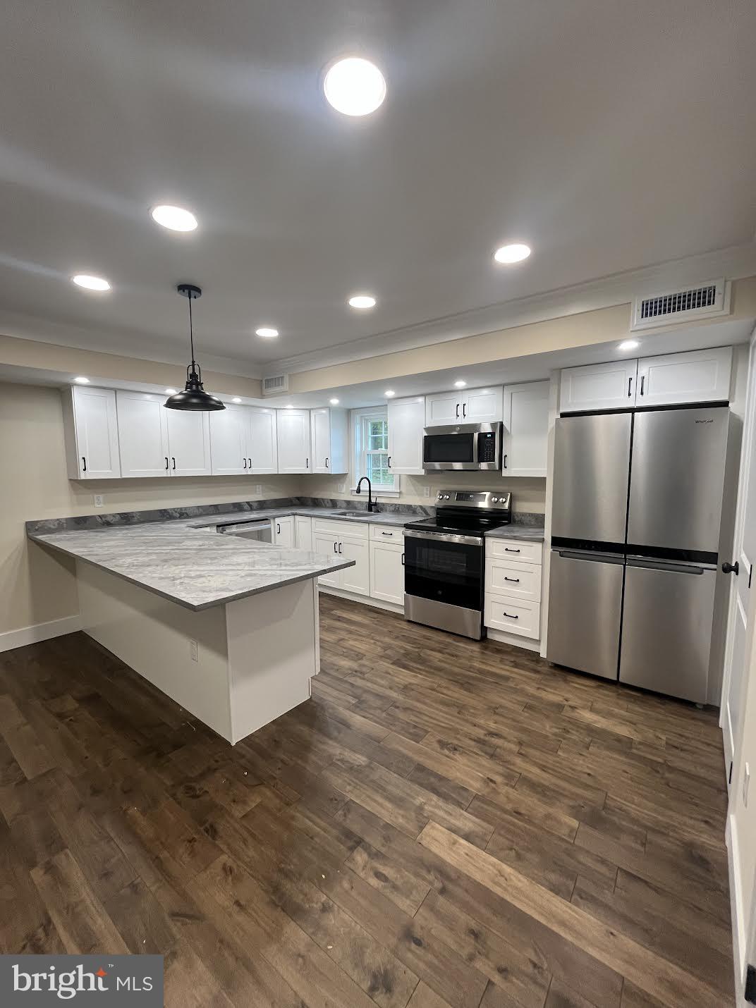 a large kitchen with stainless steel appliances kitchen island a large counter top and wooden floors