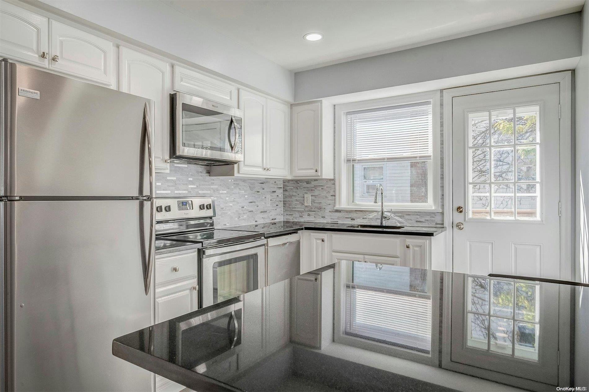 a kitchen with stainless steel appliances granite countertop a refrigerator a stove a sink and white cabinets