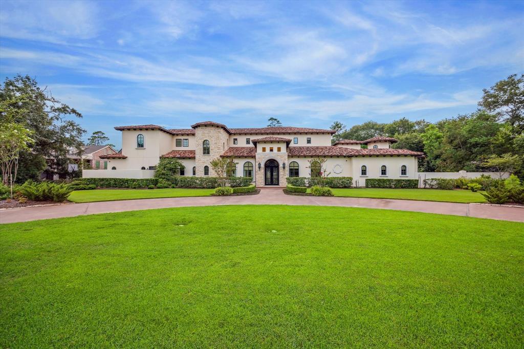 Gated Mediterranean estate home features stucco walls, clay tile roof, arched doorways & windows, stone accents. The front entry is slightly recessed and framed by a pair of columns and an arched doorway with intricate wrought ironwork with a scroll design, adding both security and decorative detail. The dark iron contrasts nicely with the lighter stone and stucco surrounding it, making the entry door a true centerpiece. Meticulously manicured grounds frame the front exterior of the home.