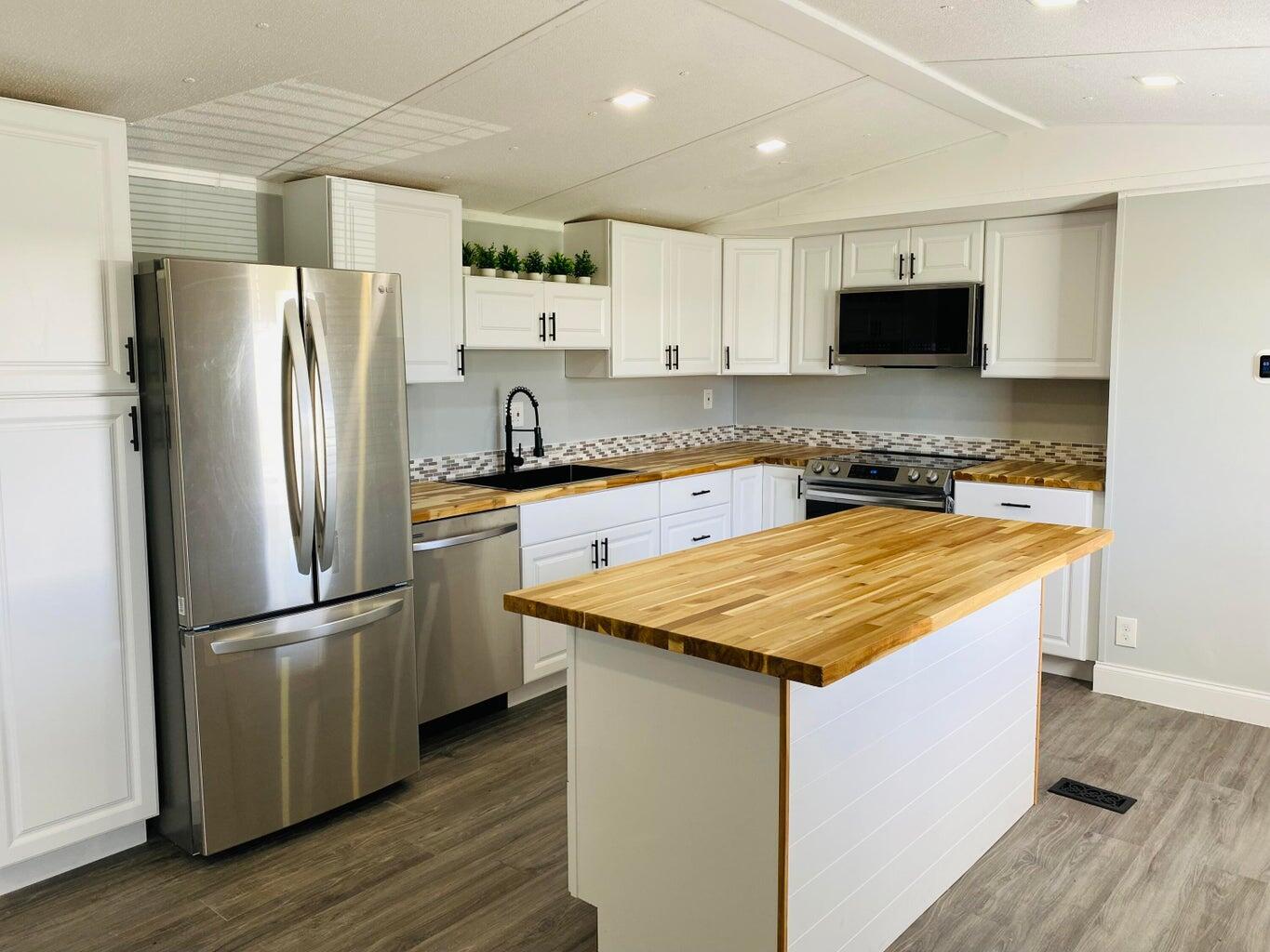 a kitchen with stainless steel appliances granite countertop a refrigerator a sink dishwasher a stove and white countertops with wooden floor