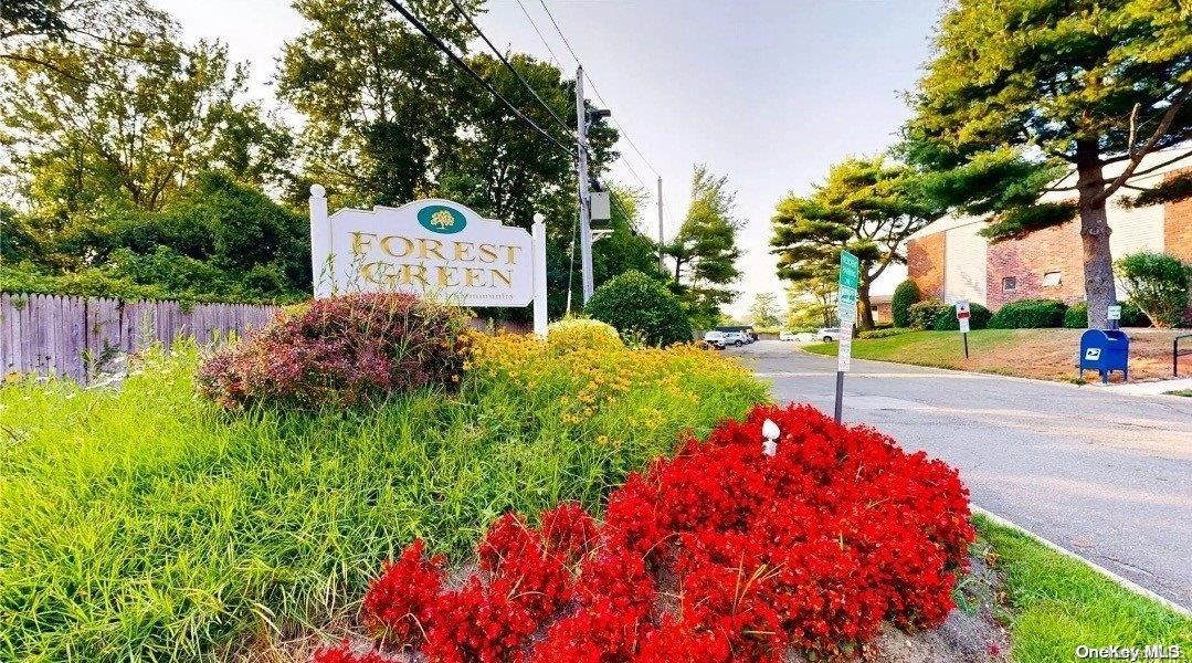 a sign board with flower plants and large trees