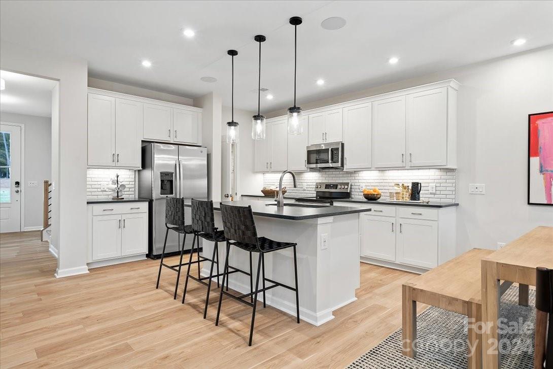 a kitchen with stainless steel appliances kitchen island granite countertop a refrigerator a stove a sink dishwasher and a dining table with wooden floor