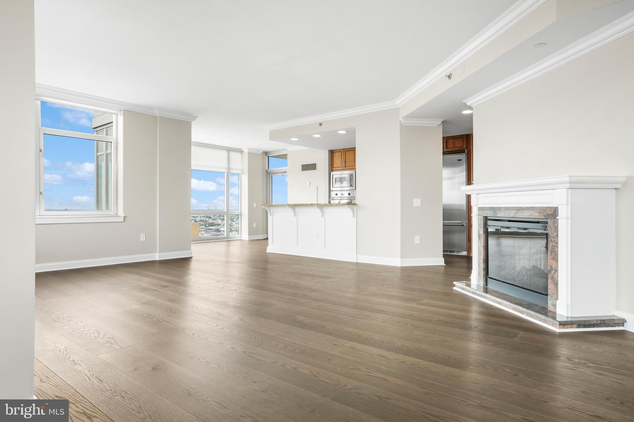 an empty room with wooden floor kitchen view and windows