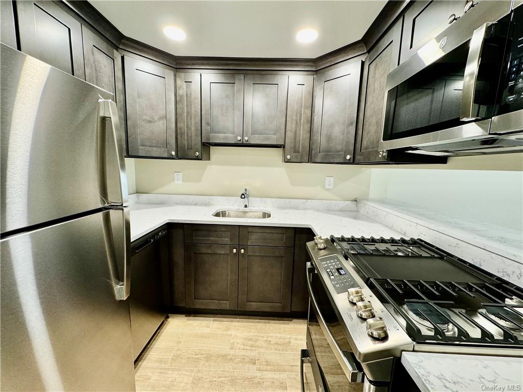 Kitchen featuring light stone counters, stainless steel appliances, sink, and dark brown cabinets