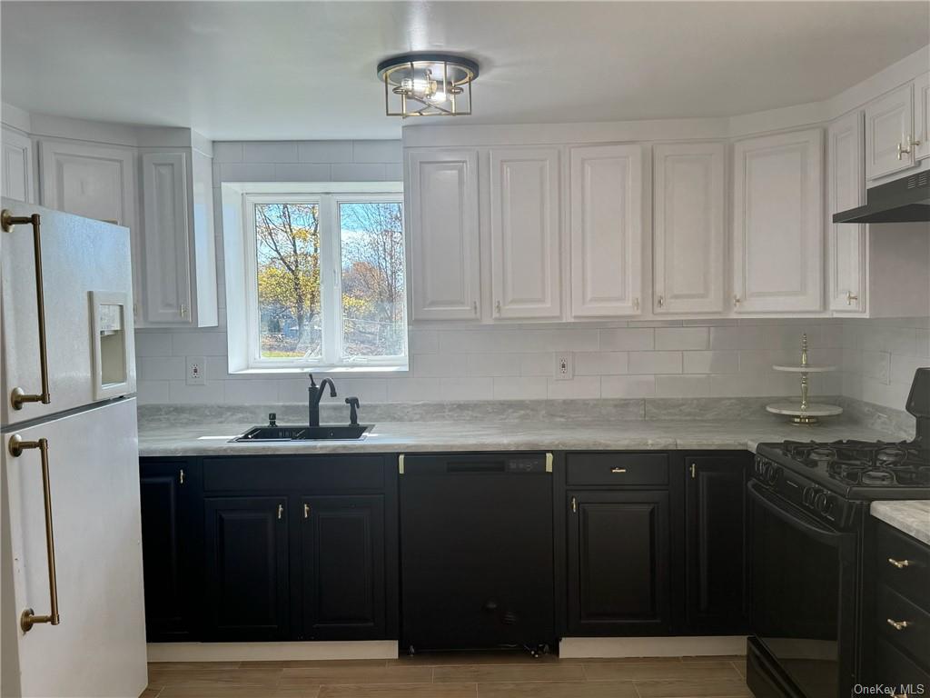 Kitchen with backsplash, sink, light stone countertops, black appliances, and white cabinetry