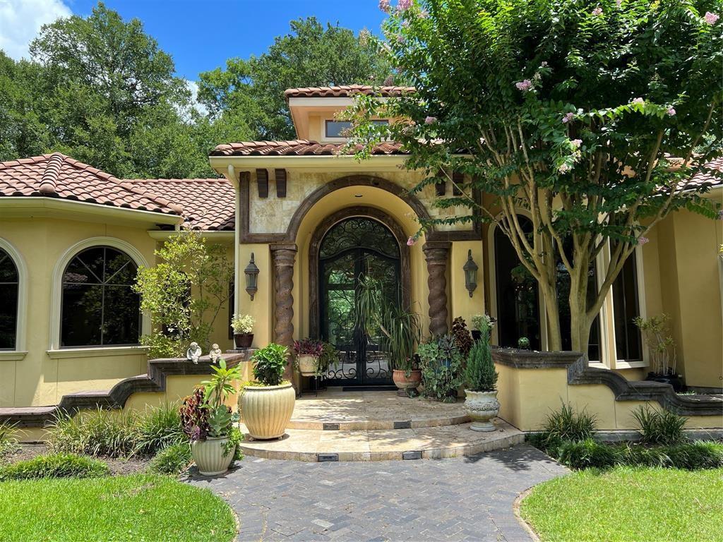 Elegant residence with travertine pavers and grand Cantera columns, embraced by lush greenery and historical charm.