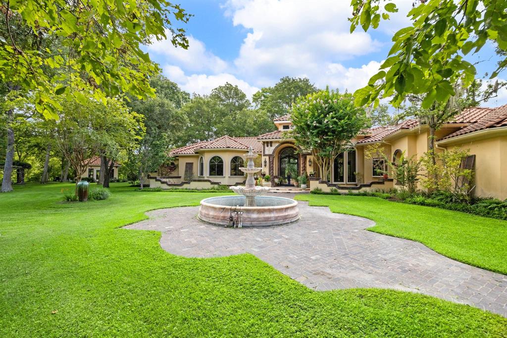 Majestic home with stone columns, travertine tiles, and a wrought iron double door entry, framed by lush greenery and elegant Terracotta tile roofing.