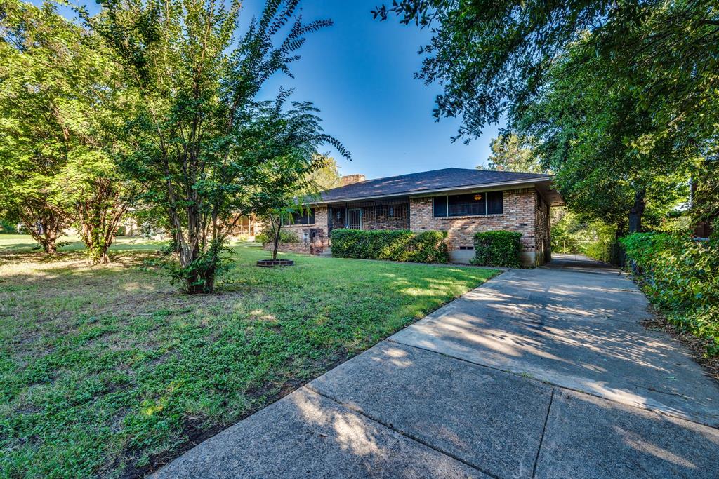 a view of house in front of a big yard with large trees