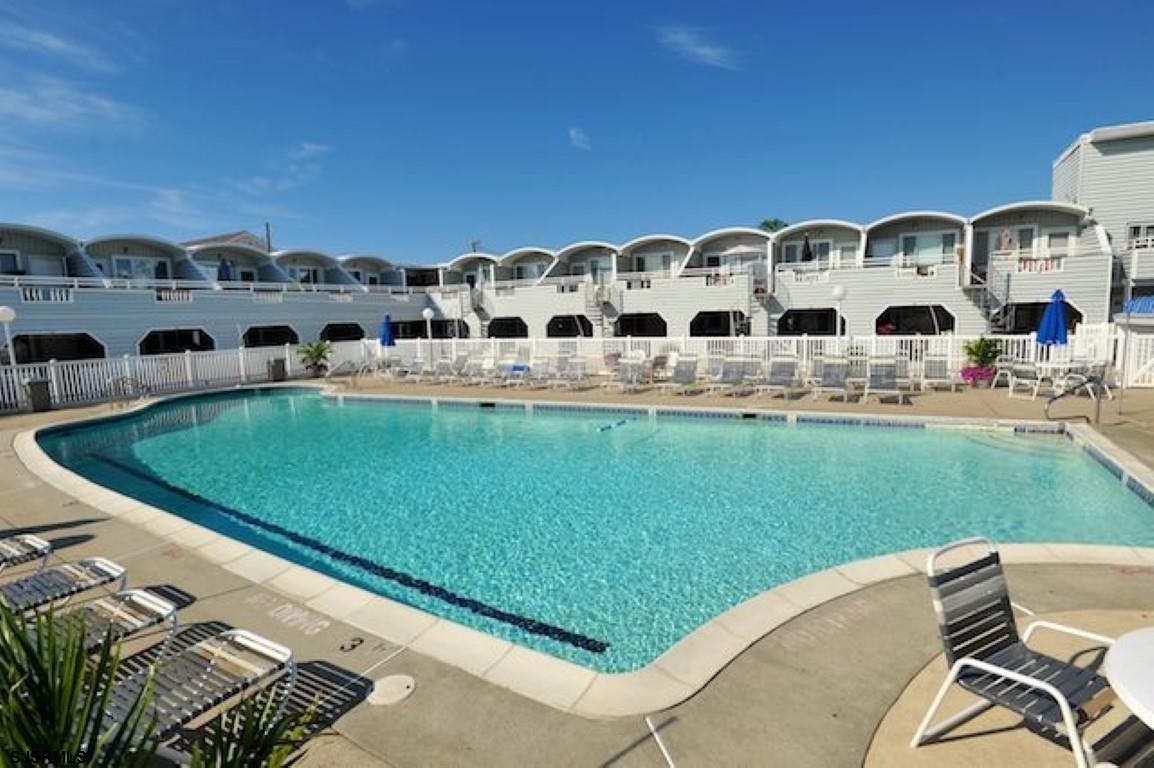 a view of a large pool with lawn chairs and a big yard