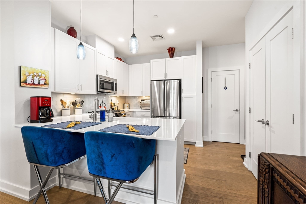 a living room with stainless steel appliances kitchen island a table chairs and a refrigerator