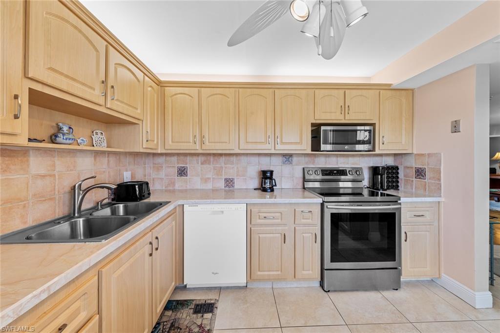 Kitchen with stainless steel appliances, light tile patterned floors, sink, and tasteful backsplash