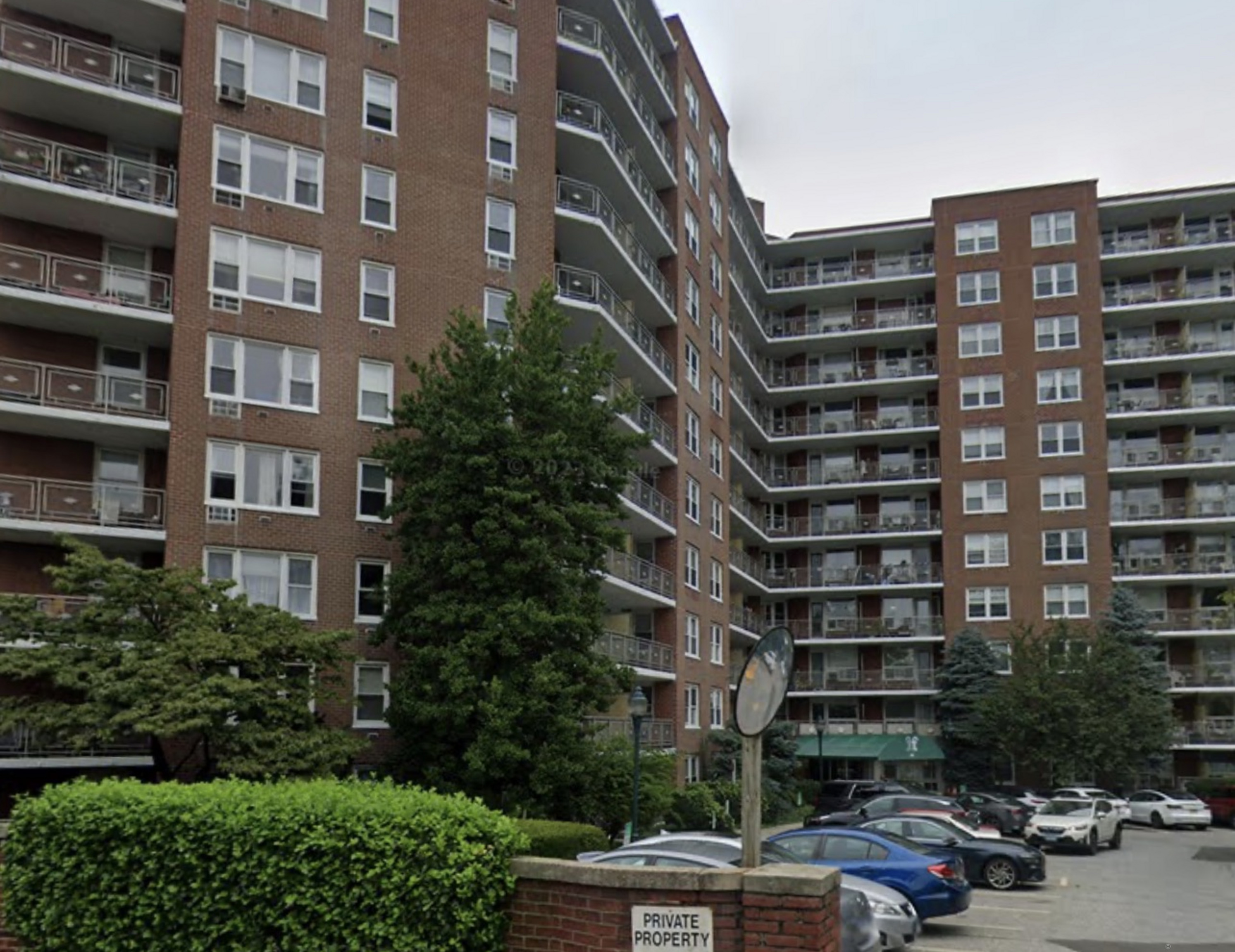 a front view of a building with lot of cars and trees