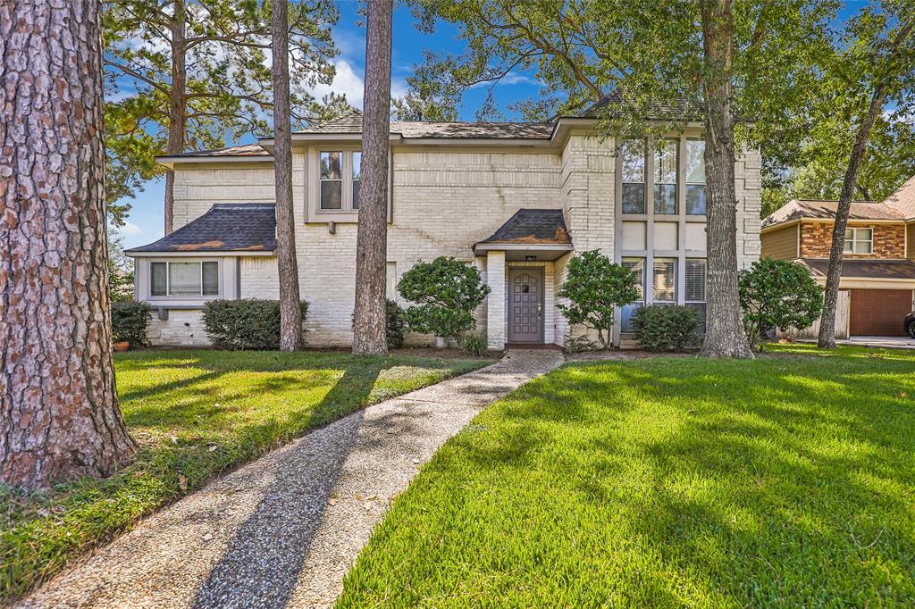 This is a two-story, traditional-style home featuring a brick facade, flanked by mature trees, with a welcoming pathway to the front door and a well-manicured lawn.