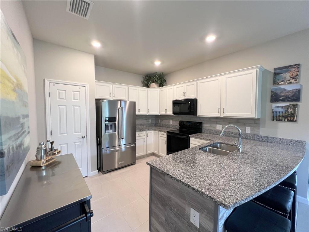 Kitchen featuring black appliances, kitchen peninsula, backsplash, sink, and light tile floors