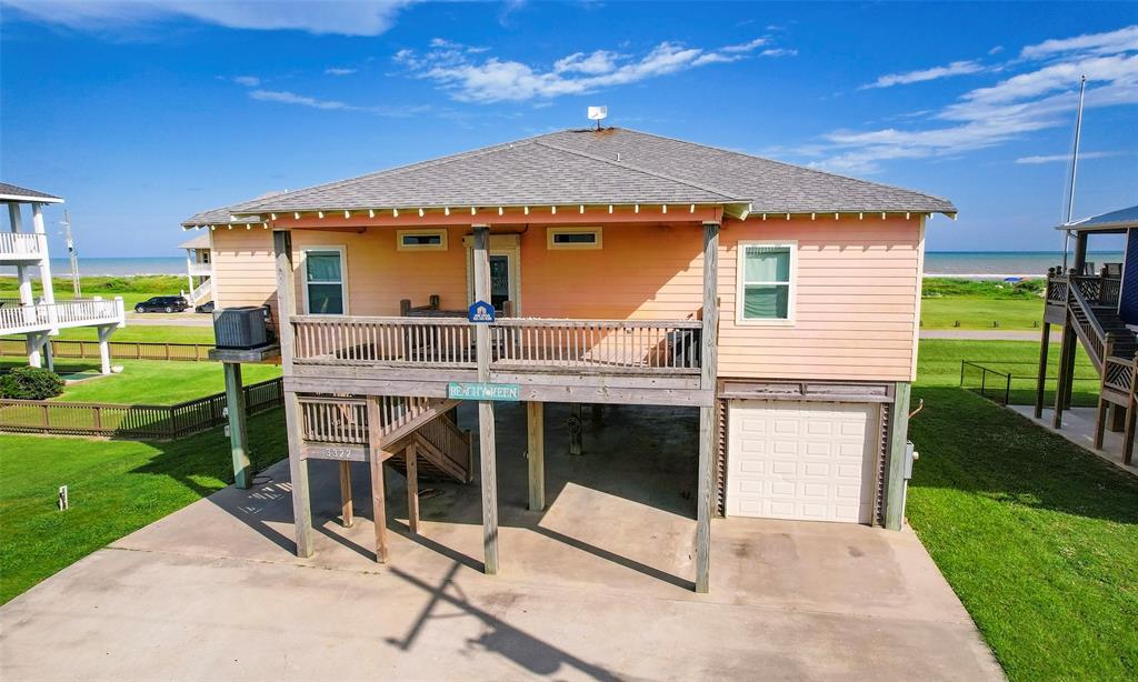 This single-story, elevated beach house with cement board exterior features a spacious wooden deck front and back, an under-house garage, and is situated in close proximity to the ocean with a clear view of the beach.