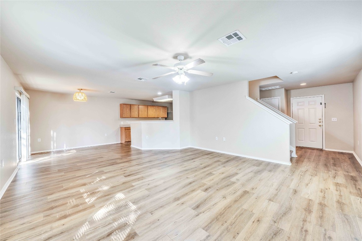 a view of an empty room with wooden floor and a ceiling fan