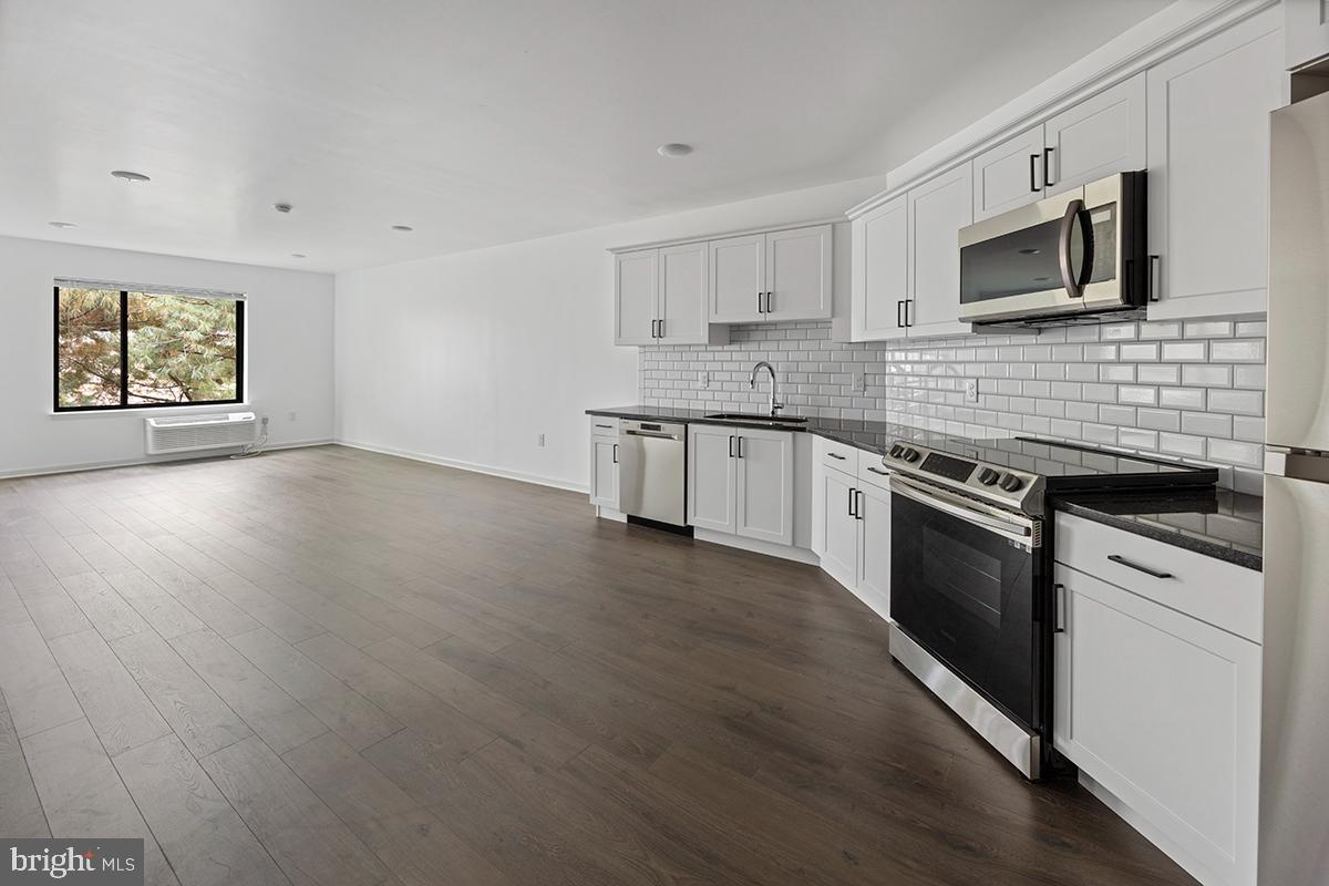 a kitchen with stainless steel appliances kitchen island granite countertop a stove top oven a sink dishwasher and a microwave oven on the wooden floor