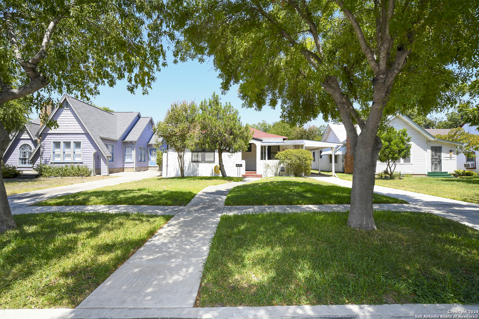 a view of house in front of a big yard with large trees