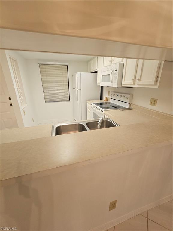 Kitchen with white fridge, light tile patterned flooring, stainless steel range, and white cabinets