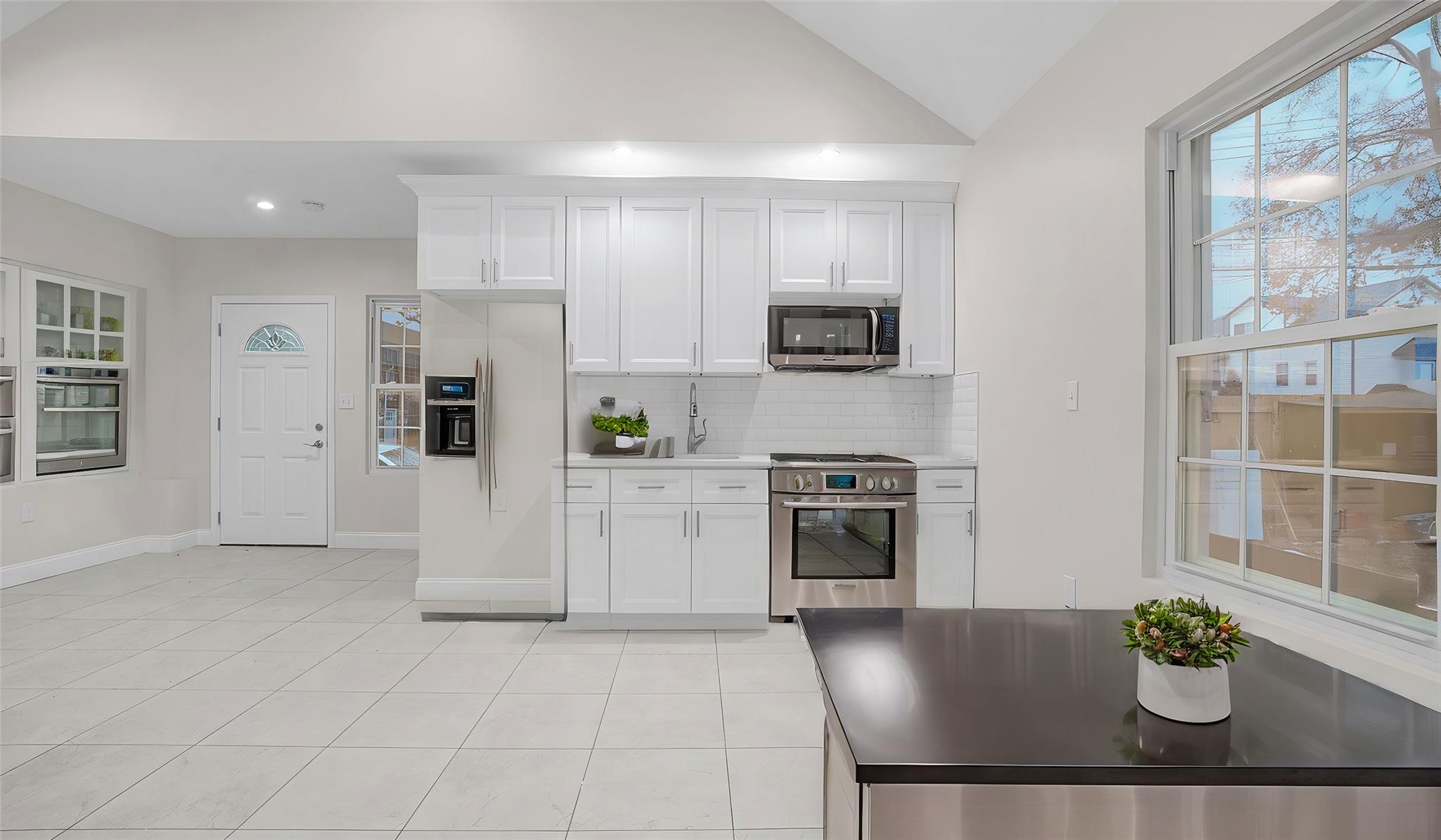 Kitchen with white cabinets, backsplash, lofted ceiling, light tile patterned floors, and appliances with stainless steel finishes