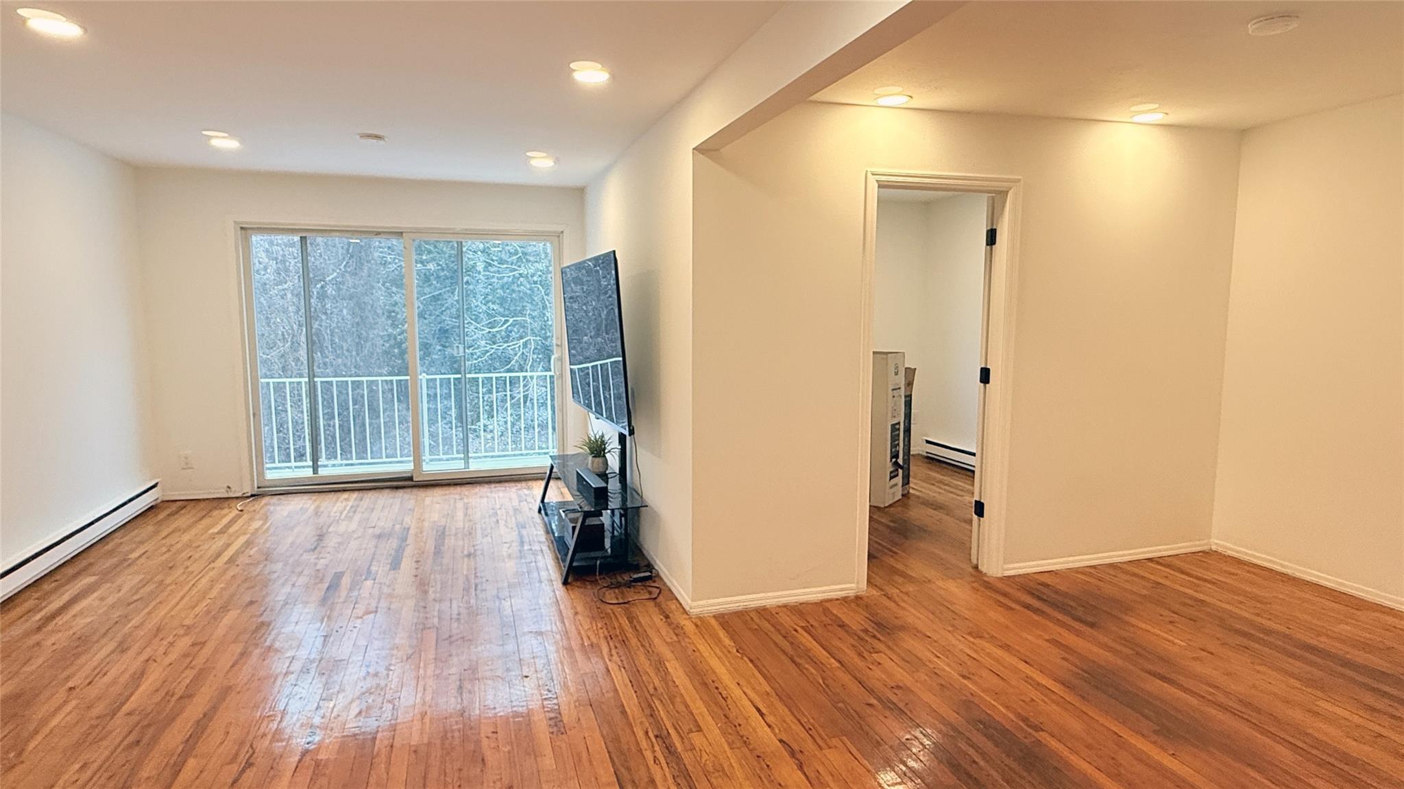 Empty room featuring wood-type flooring and a baseboard radiator