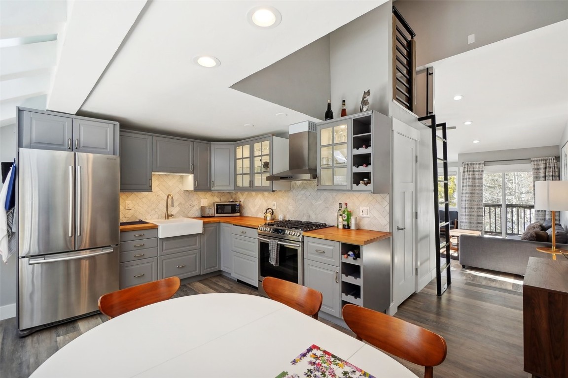 Kitchen with butcher block counters, sink, stainless steel appliances, wall chimney range hood, and dark hardwood / wood-style flooring