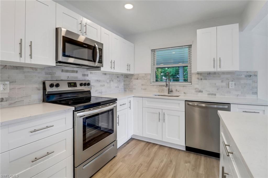 a kitchen with stainless steel appliances white cabinets a sink a stove a microwave and wooden floors